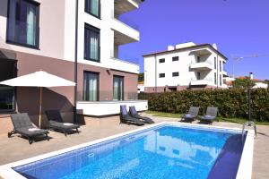 a swimming pool with chairs and an umbrella next to a building at Luxury apartment Faro with sea view and swimming pool in Premantura