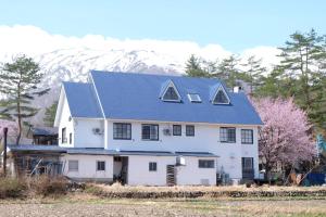 a white house with a blue roof with mountains in the background at Hakuba Snow Fox in Hakuba