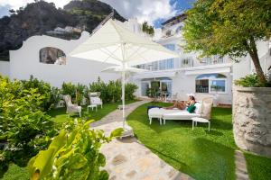 Una donna seduta su un divano sotto un ombrello in un giardino di Villa Francesco Luxury Suites a Positano