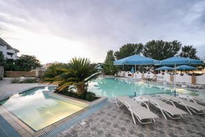 a swimming pool with white chairs and blue umbrellas at Estia hotel in Fourka
