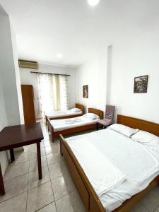 Habitación con 3 camas, mesa y escritorio. en Hostel Casa Mia SR en Sarandë