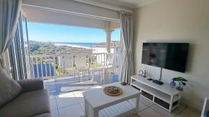 een woonkamer met een bank, een tv en een balkon bij Hello Holiday at 4 Boboyi Mangrove Beach Estate in Port Shepstone