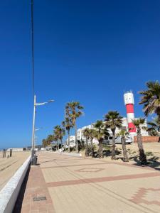 a sidewalk next to a beach with palm trees and a lighthouse at Estudio Playa Barbate in Barbate