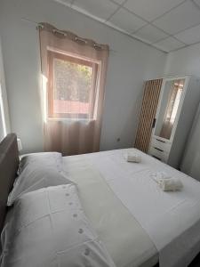 a white bedroom with two beds and a window at Apartman Daisy in Slatine