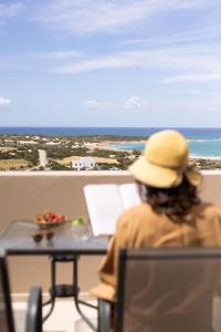 een vrouw aan een tafel die uitkijkt op de oceaan bij Panorama Suites in Kastraki Naxou