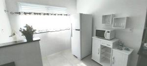 Il comprend une cuisine blanche équipée d'un réfrigérateur et d'un four micro-ondes. dans l'établissement BrotasApart - apto inteiro, à Brotas
