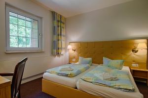 a bedroom with two beds and a desk and a window at See Hotel Karlslust Chalets in Storkow