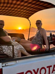 dwie kobiety siedzące z tyłu łodzi o zachodzie słońca w obiekcie Wadi Rum sky Camp w mieście Wadi Rum