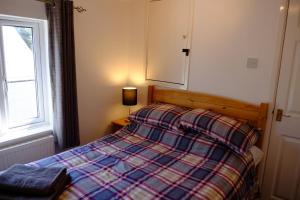 um quarto com uma cama com um cobertor xadrez e uma janela em Cosy Cottage to Relax or Explore em Mistley