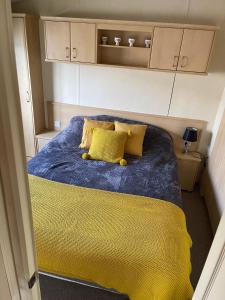a small room with a bed with yellow pillows at 6 berth Seawick Caravan Park, St Osyth in Colchester