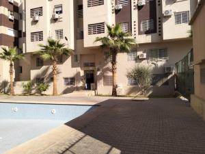 馬拉喀什的住宿－Les portes de Gueliz - apartment 6 people，一座棕榈树环绕的建筑,位于游泳池前