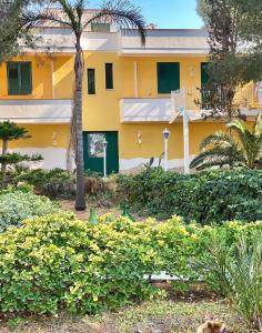 a yellow building with a palm tree and bushes at Villa Lu in Porto Cesareo