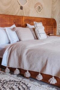 - un lit avec des oreillers blancs et une tête de lit en bois dans l'établissement Caravanserai Luxury Desert Camp, à Merzouga
