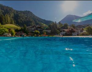 een groot zwembad van blauw water met bergen op de achtergrond bij Pension Felseneck in San Leonardo in Passiria