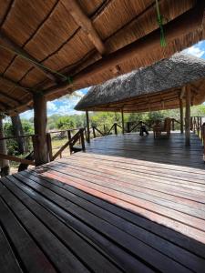 una terraza de madera con techo de paja y mesa en Bua River Lodge 
