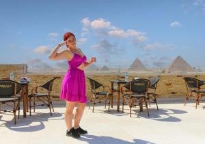 pyramids guest house في القاهرة: امرأة ترتدي ثوب وردي تقف أمام الاهرامات