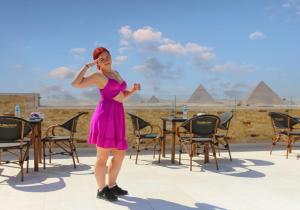 een vrouw in een roze jurk die voor piramiden staat bij pyramids guest house in Caïro