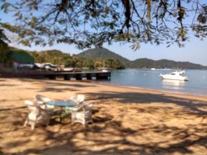a table and chairs on a beach with a boat at Mansao Angra Pe na Areia in Angra dos Reis