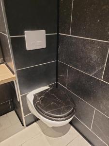 a black tiled bathroom with a toilet with a brown seat at La Cabane Enchanteresse in Illoud