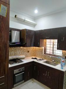 cocina con armarios de madera, fogones y fregadero en Balqees Cottage en Lahore