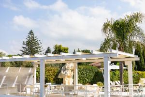 a white pergola with white chairs and palm trees at L' Arcobaleno Resort in Capo Vaticano
