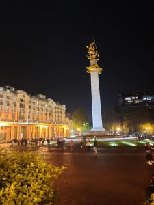 Una gran torre con una estatua encima por la noche. en Apartment tbilisi central, en Tiflis