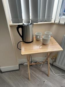 una cafetera sentada en una mesa de madera con dos tazas en ELSARO guest house en Slough