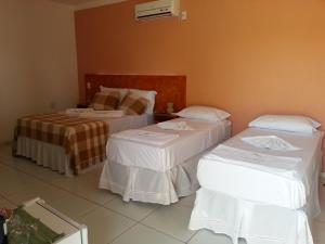 two beds in a hotel room with white sheets at Pousada Brisa Do Pontal in Fortim