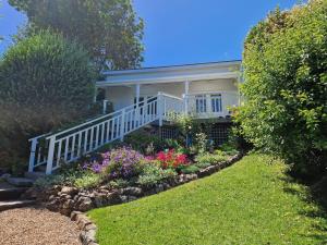 a house with a white porch and some flowers at Romantic Cottage Recommended by NZ Herald in Oneroa