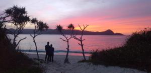 una pareja de pie en la playa viendo la puesta de sol en umidaisyou-海大将-, 