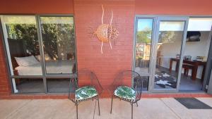 two chairs sitting in front of a red brick wall at Red Ochre – Large 1BR with Private Courtyard in Port Pirie