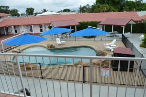 un uomo sdraiato in una piscina con ombrelloni blu di Monte Carlo Motor Inn a Townsville