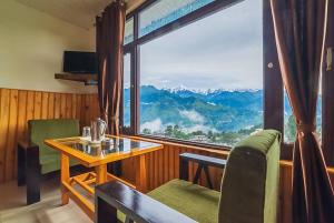 een kamer met een tafel en stoelen en een groot raam bij Goroomgo Bala Paradise Munsyari - Himalayan View Room in Munsyari