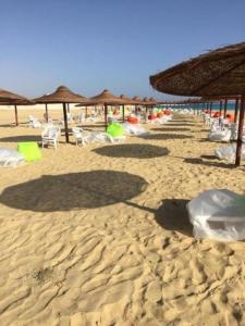 a sandy beach with umbrellas and chairs and tables at luxury 3BD villa in Stella Heights - North Coast فيلا فاخره ستيلا هايتس الساحل الشمالي in El Alamein
