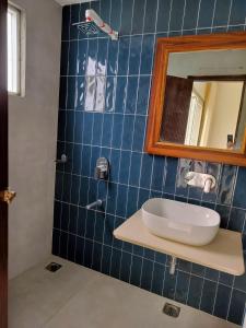 La salle de bains est pourvue de carrelage bleu, d'un lavabo et d'un miroir. dans l'établissement Hotel Aaria, à Mussoorie