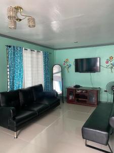 sala de estar con sofá de cuero negro y TV de pantalla plana en AB Yam Staycation Gensan near Venue88, en General Santos