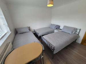 a group of three beds in a room with a table at GATWICK ROOMs in Ifield