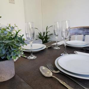 una mesa con platos blancos y copas de vino. en AnchorageWells Cottage for 8 to 10 people, en Wells-next-the-Sea