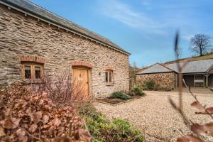 a stone house with a wooden door in a yard at The Cowshed in Clatworthy