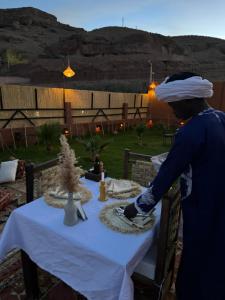 una mujer de pie en una mesa con un mantel blanco en Riad Sahara Stars Dades, en Boumalne