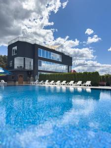 a building with a swimming pool with white lounge chairs at Avalon Hotel&Pool in Yelikhovichi