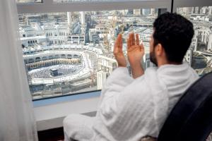 een man in een stoel die uit een raam naar een stadion kijkt bij Swissotel Makkah in Mekka
