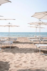 a row of beach chairs with umbrellas on a beach at Hotel Capri 3 Stelle SUPERIOR in Lido di Jesolo
