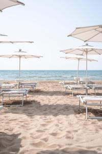 una fila de sillas de playa con sombrillas en una playa en Hotel Capri 3 Stelle SUPERIOR, en Lido di Jesolo