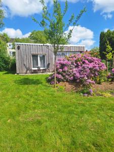 a shed with a tree in a yard with purple flowers at Ferienhaus Marie an der Weser in Bremerhaven