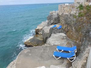 three blue lounge chairs sitting on a cliff near the ocean at home sweet home resort in Negril