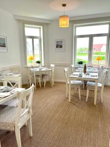 a dining room with white tables and chairs and windows at Hotel Villa Klasen in Wenningstedt