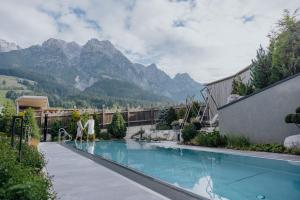 a couple standing next to a swimming pool with mountains at Hotel Riederalm in Leogang