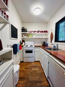 a white kitchen with a sink and a stove at Waterfront Chalet Serendipity Hideaway - Cachette Sérendipité - Swim SUPs BBQ Relax w Wifi in Chertsey