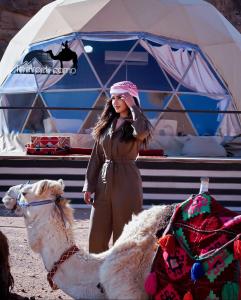 Una donna in piedi accanto a un cammello davanti a una tenda di The Rock Camp a Wadi Rum